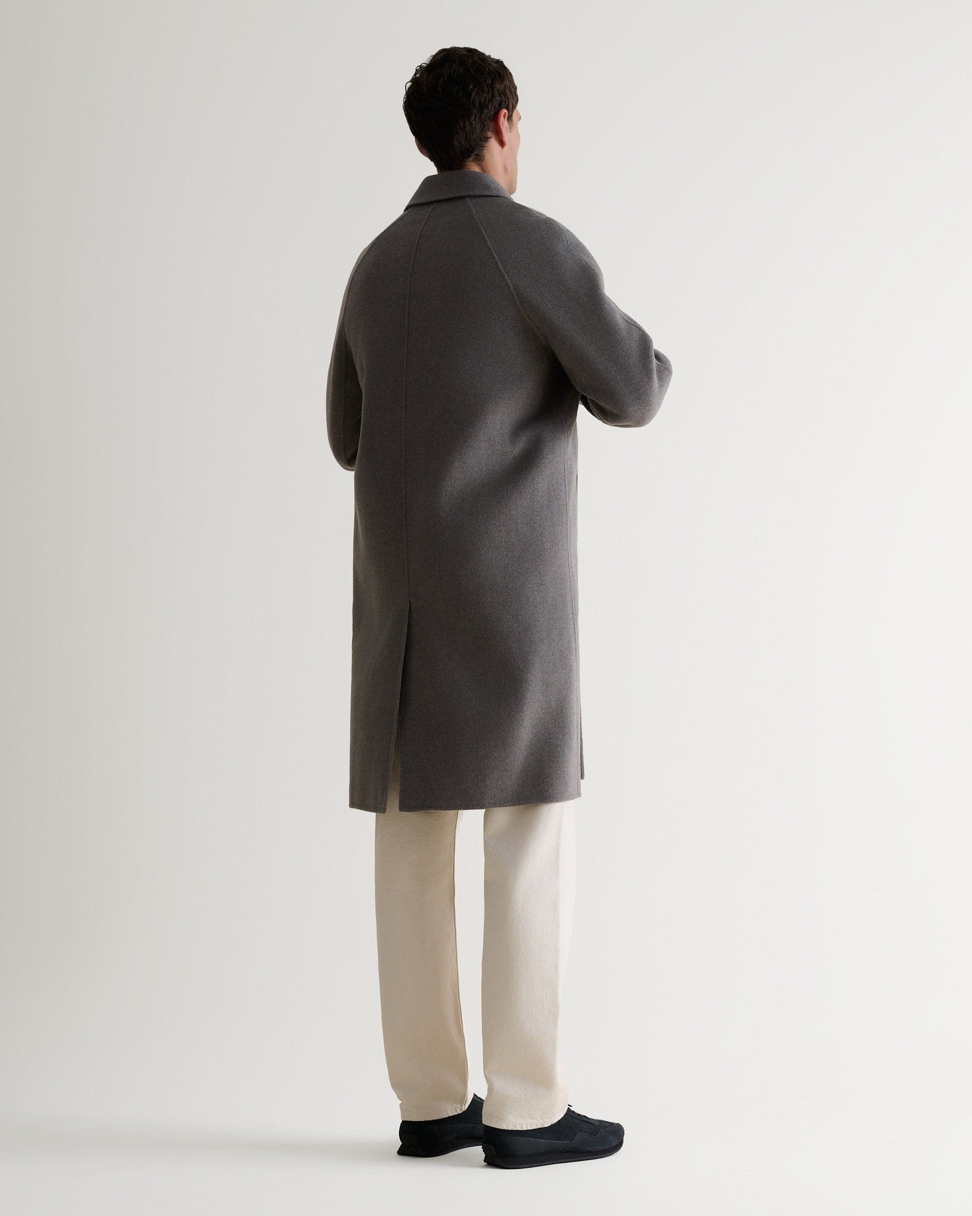 Full length back view of man wearing grey cashmere merino wool double-faced coat. Paired with cream jeans.