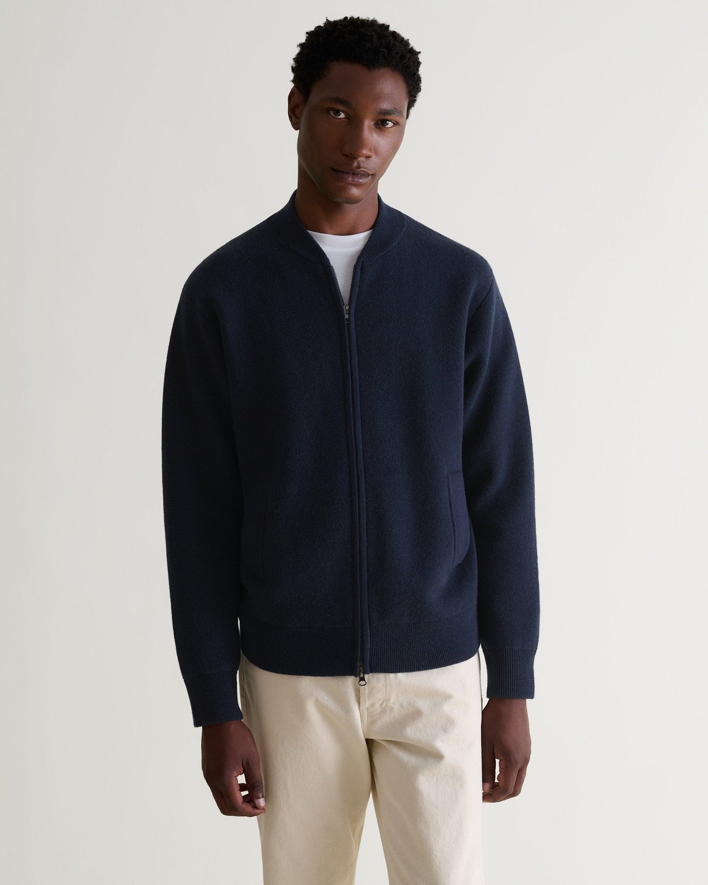 Front view of man wearing navy cashmere merino double-faced knitted bomber with cream trousers and white T-shirt.
