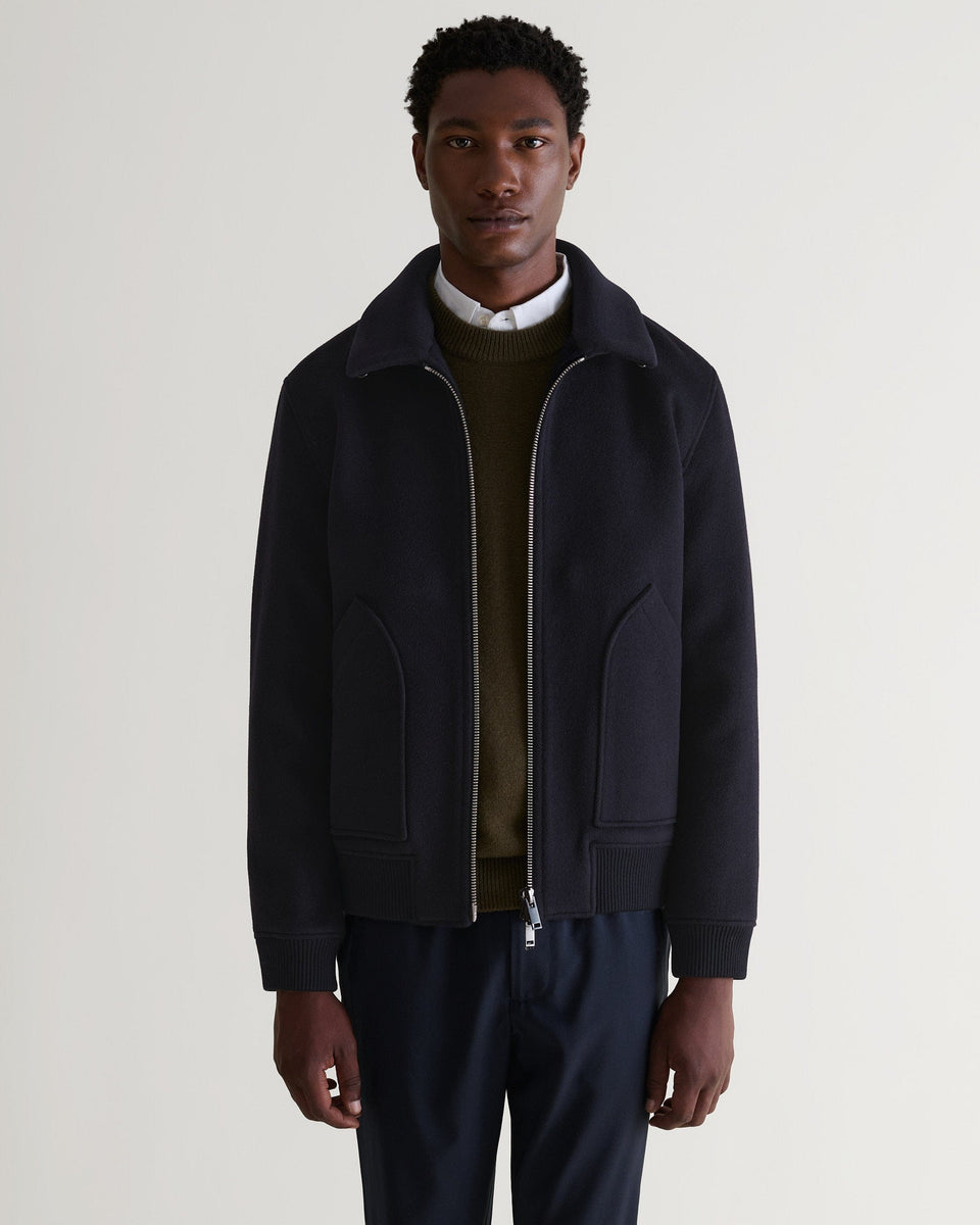 Front view of man wearing navy wool bomber jacket with shearling collar. Matched with white shirt and green jumper.