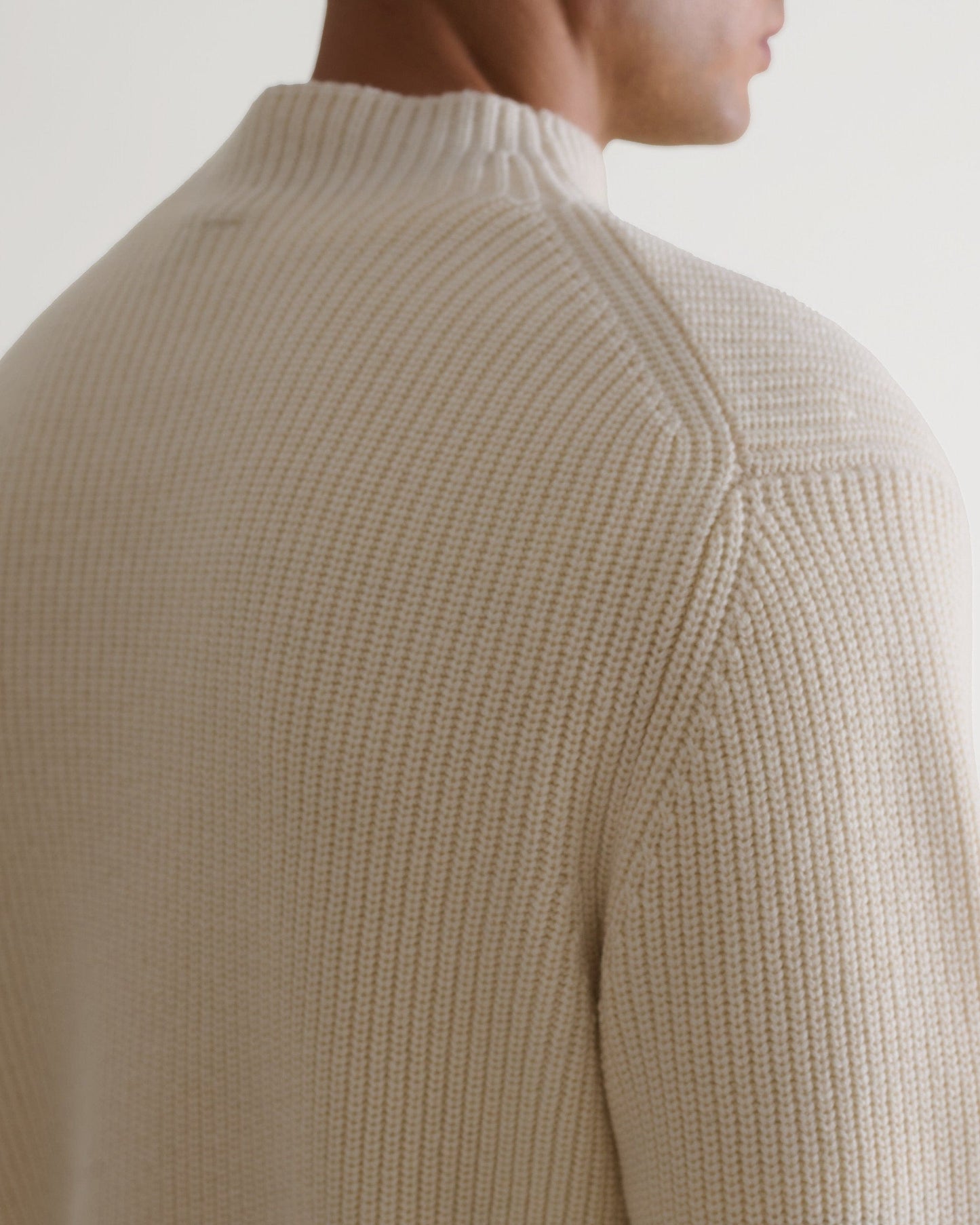 Man wears Rise & Fall's cream cashmere merino stand neck jumper. A close up of shoulder. 