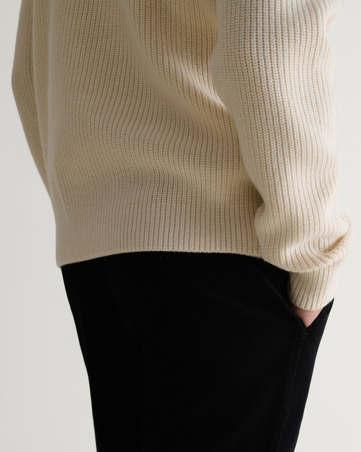 Close up side view of man wearing Rise & Fall's cream cashmere merino stand neck jumper with black trousers.