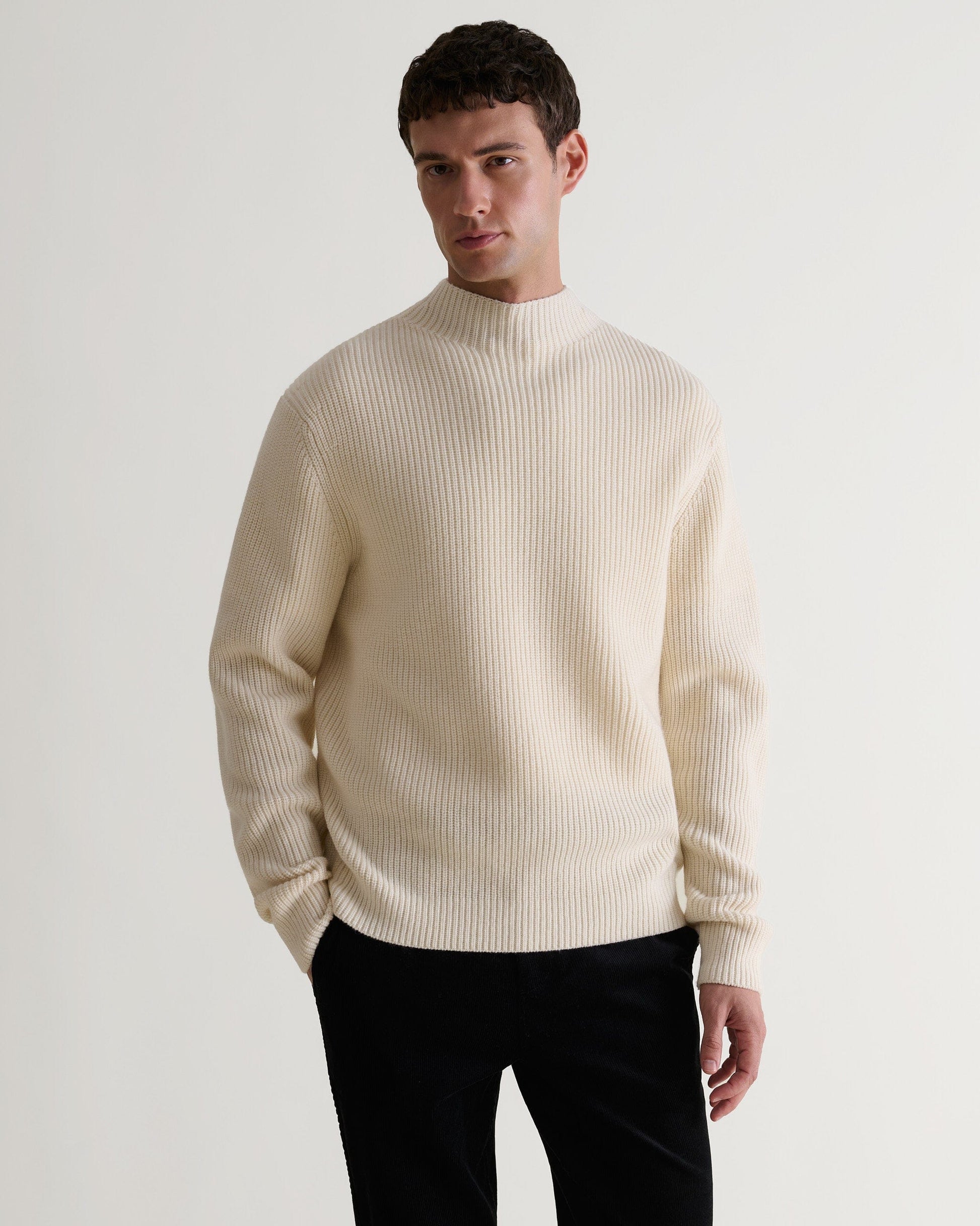 Front view of man wearing Rise & Fall's cream cashmere merino stand neck ribbed jumper with black trousers.