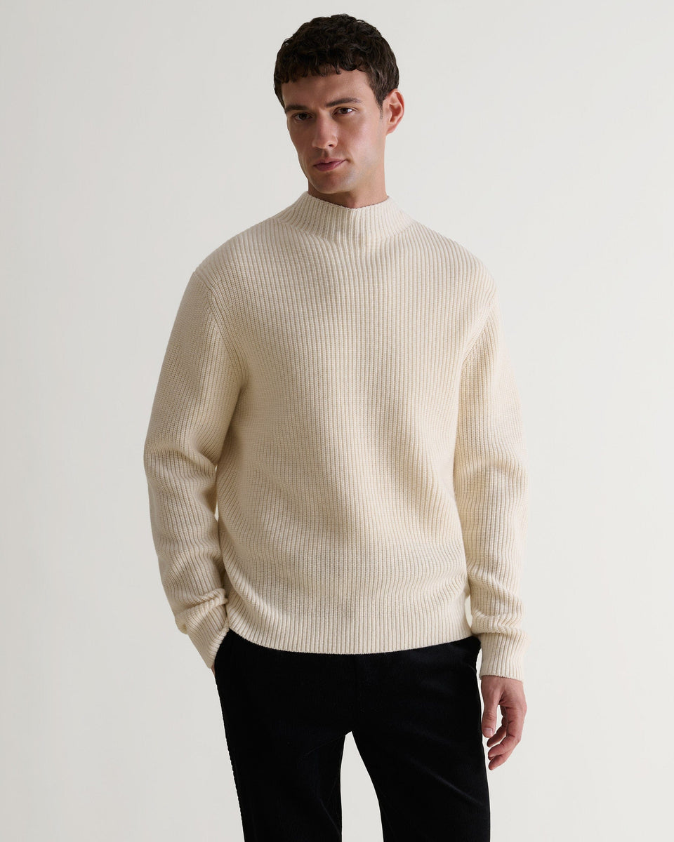Front view of man wearing Rise & Fall's cream cashmere merino stand neck ribbed jumper with black trousers.