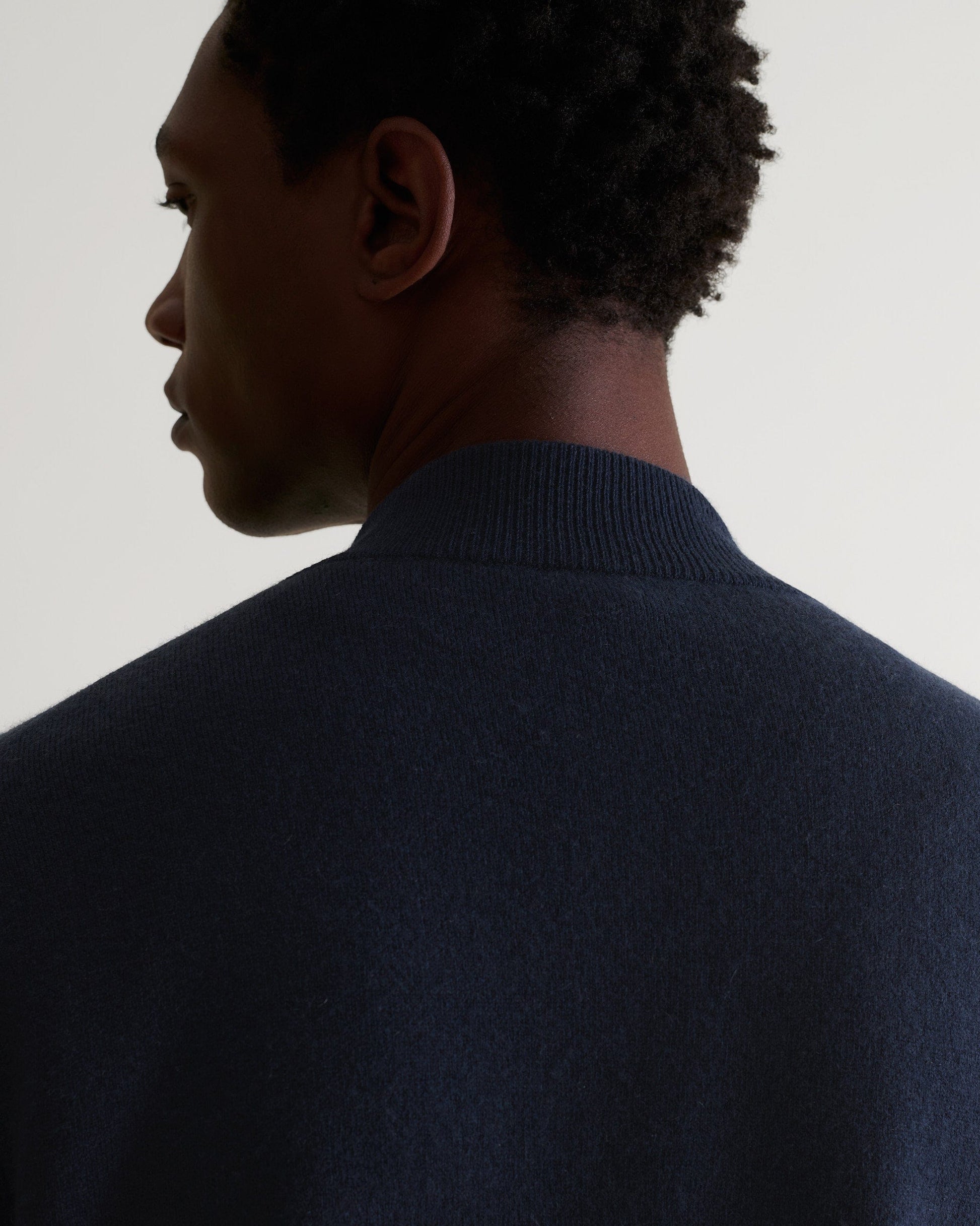 Back of man wearing Rise & Fall's navy cashmere merino double-faced knitted bomber jacket.