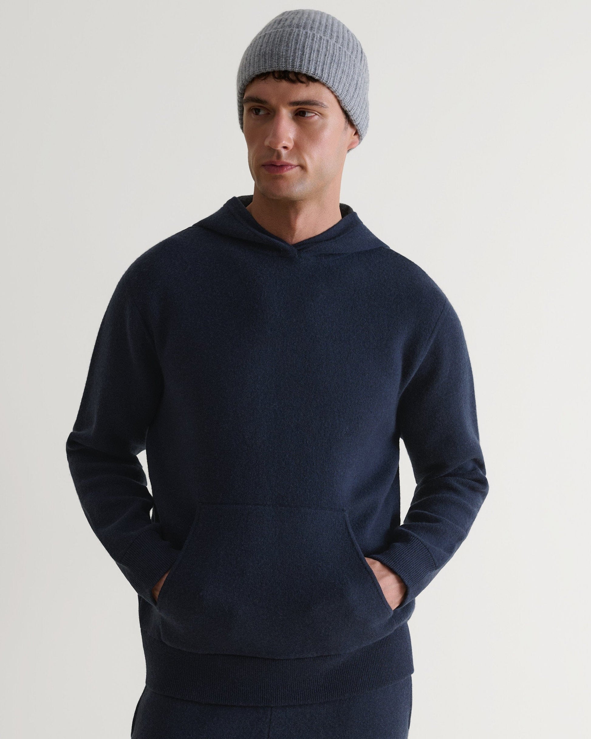 Man wears Rise & Fall's navy cashmere merino double-faced knitted hoodie with matching trousers and light grey beanie.