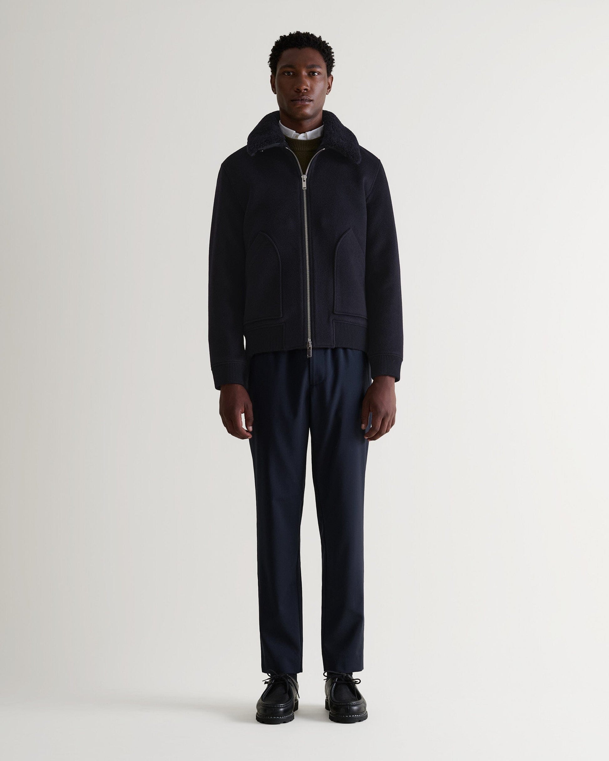 Full length front view of man wearing Rise & Fall's navy wool bomber jacket with shearling collar. Zipped up. 