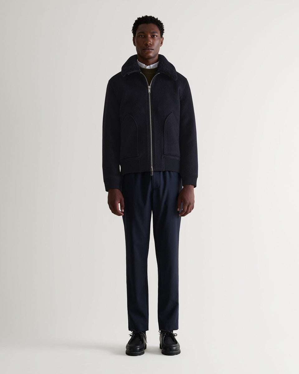 Full length front view of man wearing Rise & Fall's navy wool bomber jacket with shearling collar. Zipped up. 