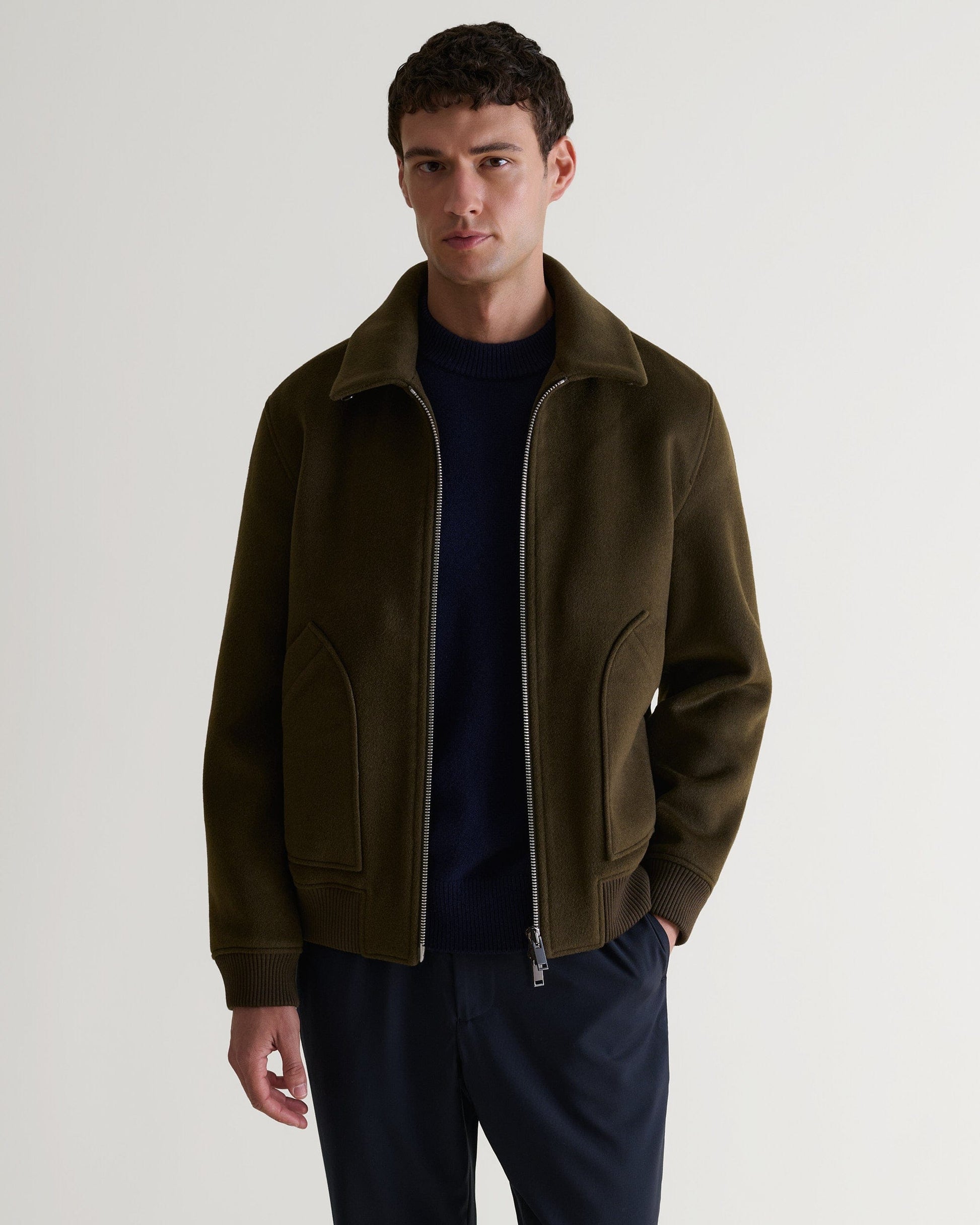 Man wears Rise & Fall's olive wool bomber jacket with shearling collar. Top half open zip.