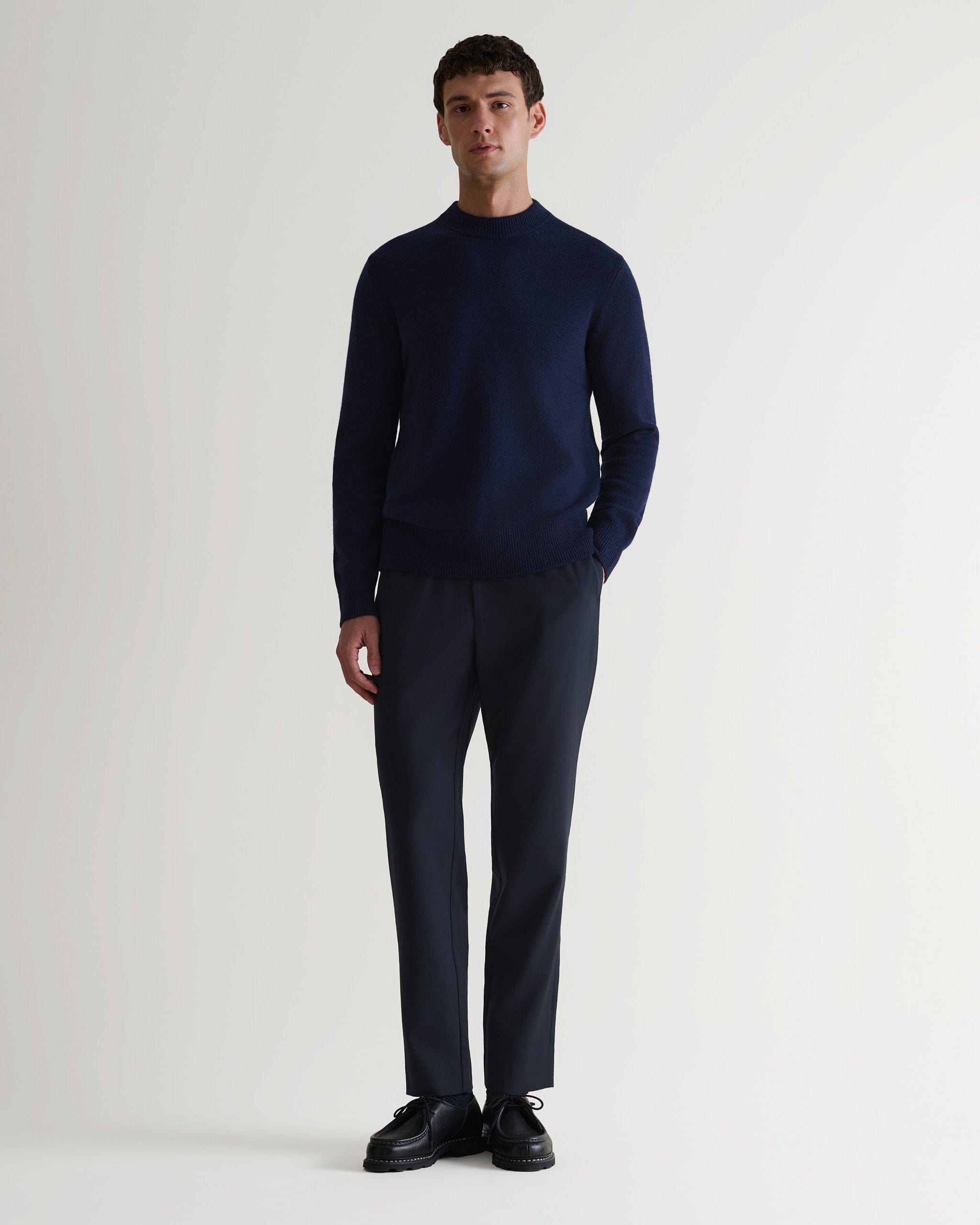 Man wears Rise & Fall's Finest Cashmere Mid-Weight Crew Neck Jumper in navy with tailored black trousers.