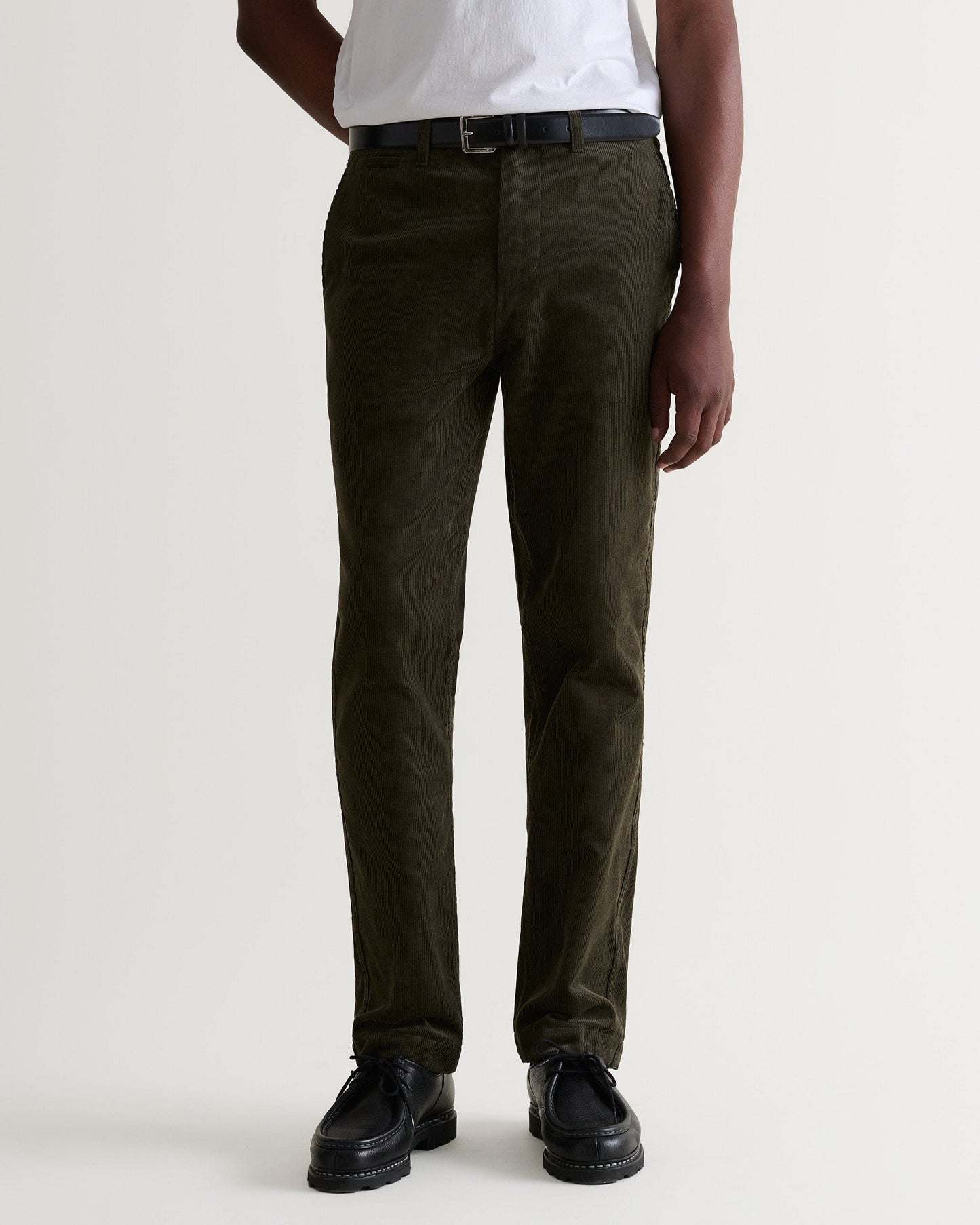 Close up front view of Rise & Fall's dark green corduroy trousers being worn with a white T-shirt and black leather belt.