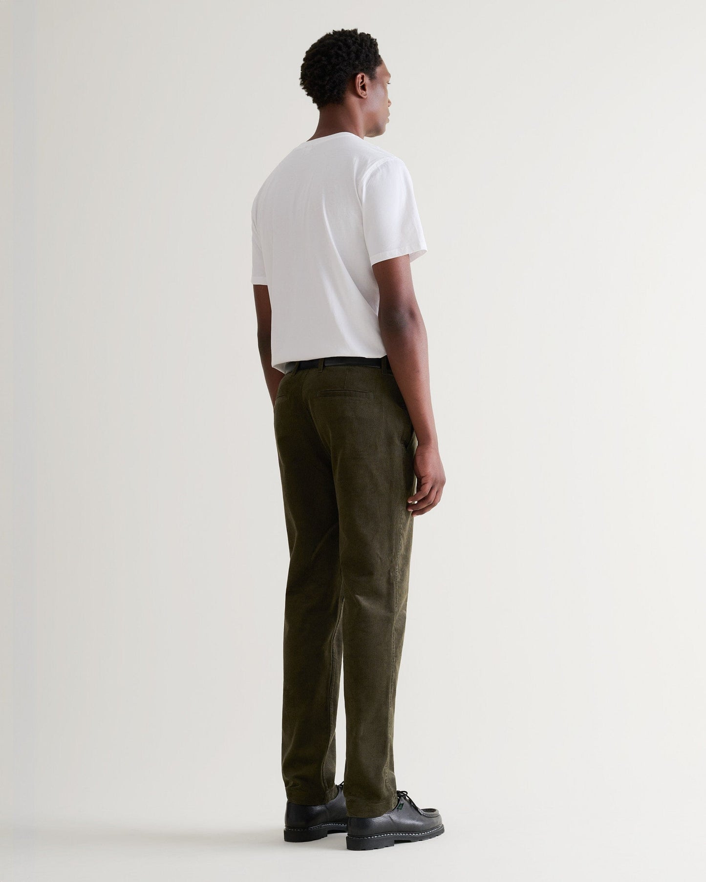 Full length back view of Rise & Fall's dark green corduroy trousers being worn with a white T-shirt and black leather shoes.