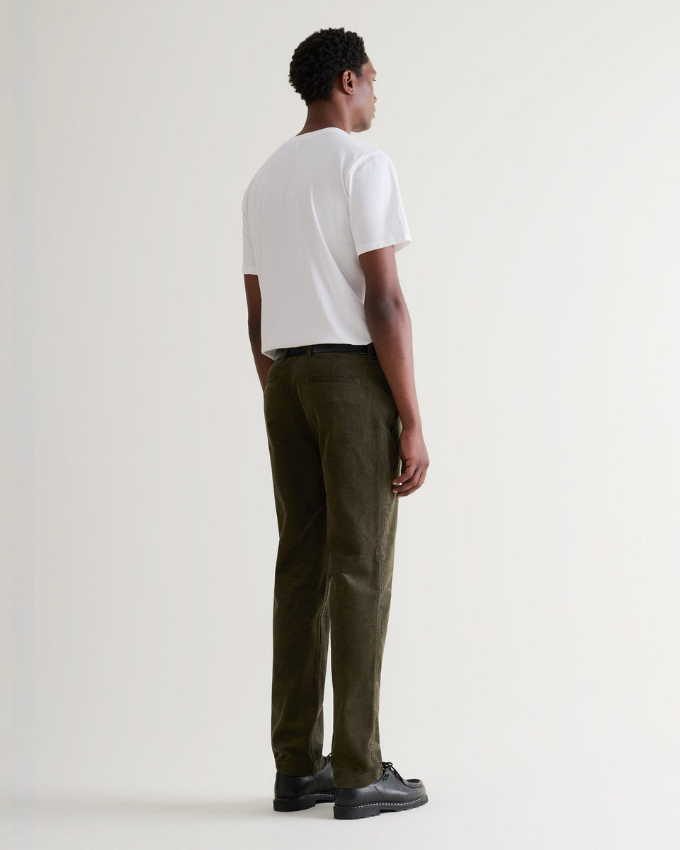 Full length back view of Rise & Fall's dark green corduroy trousers being worn with a white T-shirt and black leather shoes.