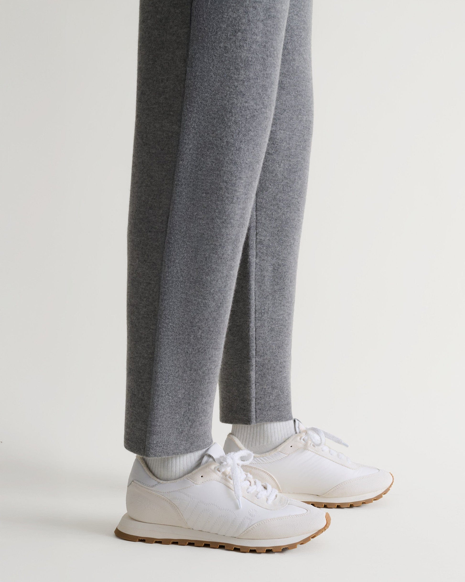 Bottom side view of Rise & Fall's grey cashmere merino double-faced joggers with white trainers. 