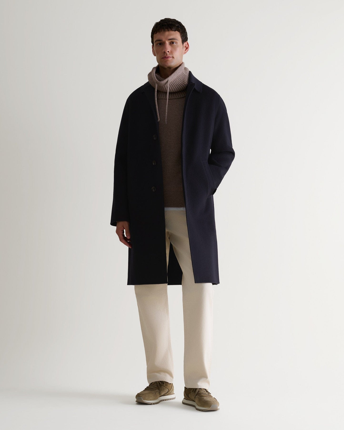Full length front view of Rise & Fall's navy cashmere merino double-faced coat. Paired with beige drawstring snood.