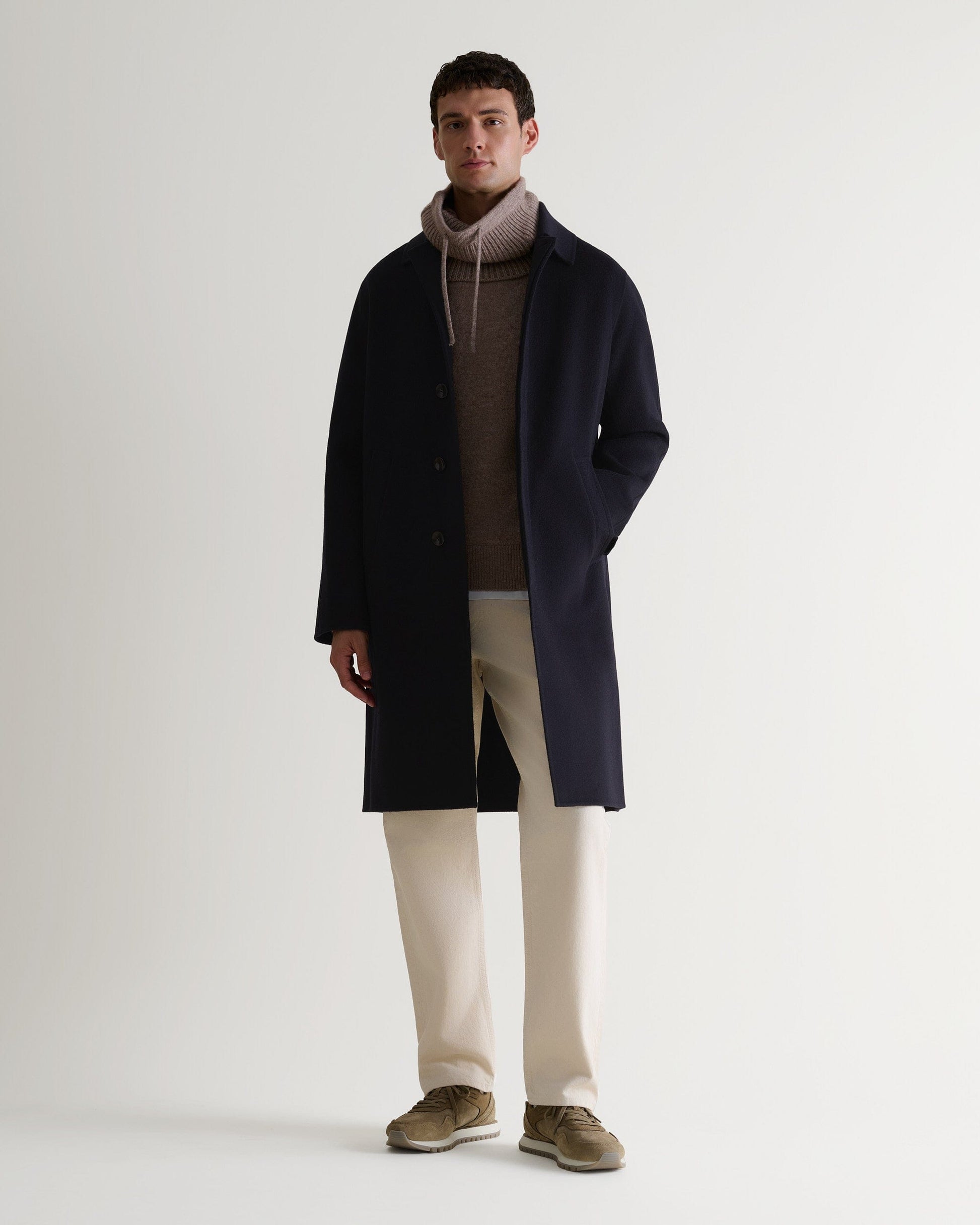 Full length front view of Rise & Fall's navy cashmere merino double-faced coat. Paired with beige drawstring snood.