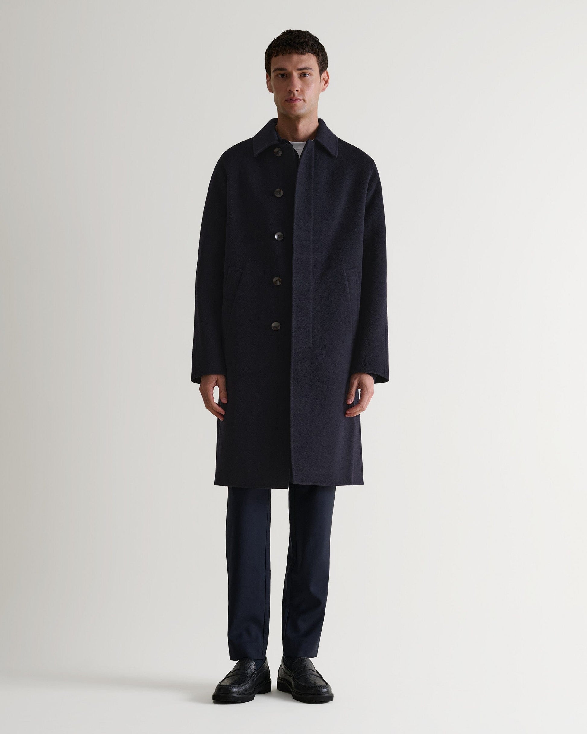 Full length front view of Rise & Fall's navy cashmere merino double-faced coat. Paired with black trousers and shoes. 