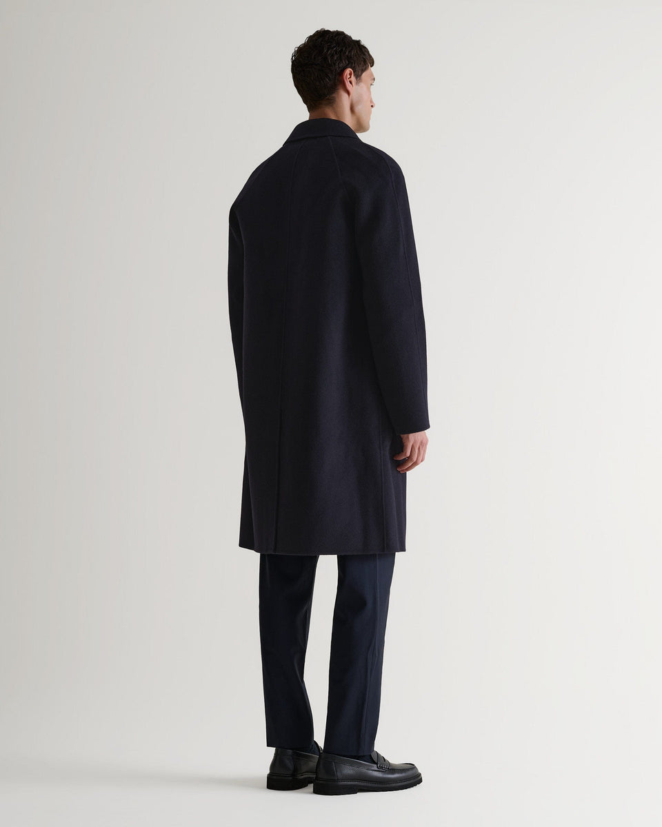 Full length back view of Rise & Fall's navy cashmere merino wool double-faced coat. Worn with black trousers and shoes.