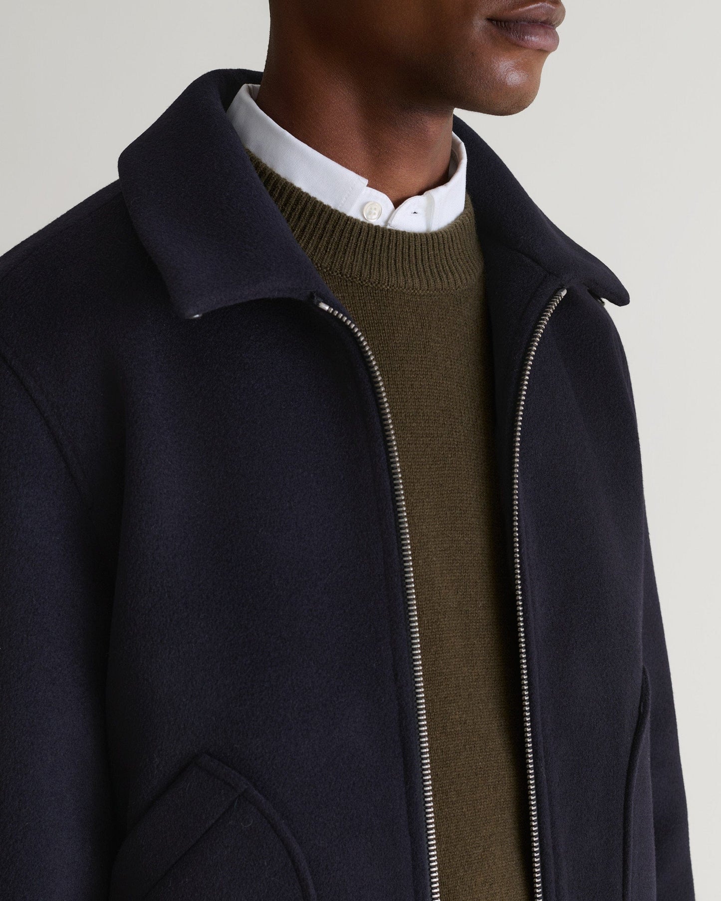 Close up side view of Rise & Fall's navy wool bomber jacket with shearling collar. Matched with white shirt and green jumper.