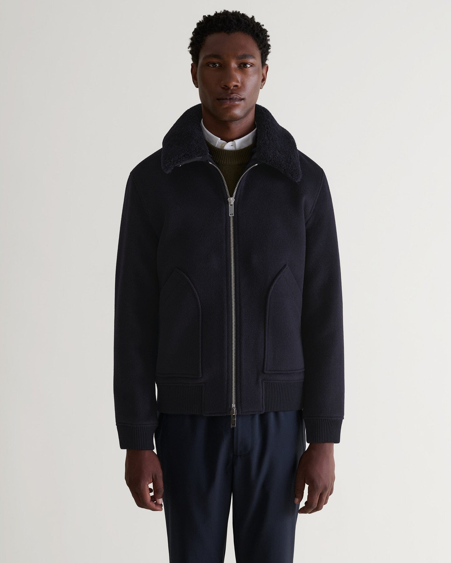 Front view of Rise & Fall's navy wool bomber jacket with shearling collar. Matched with white shirt and green jumper.