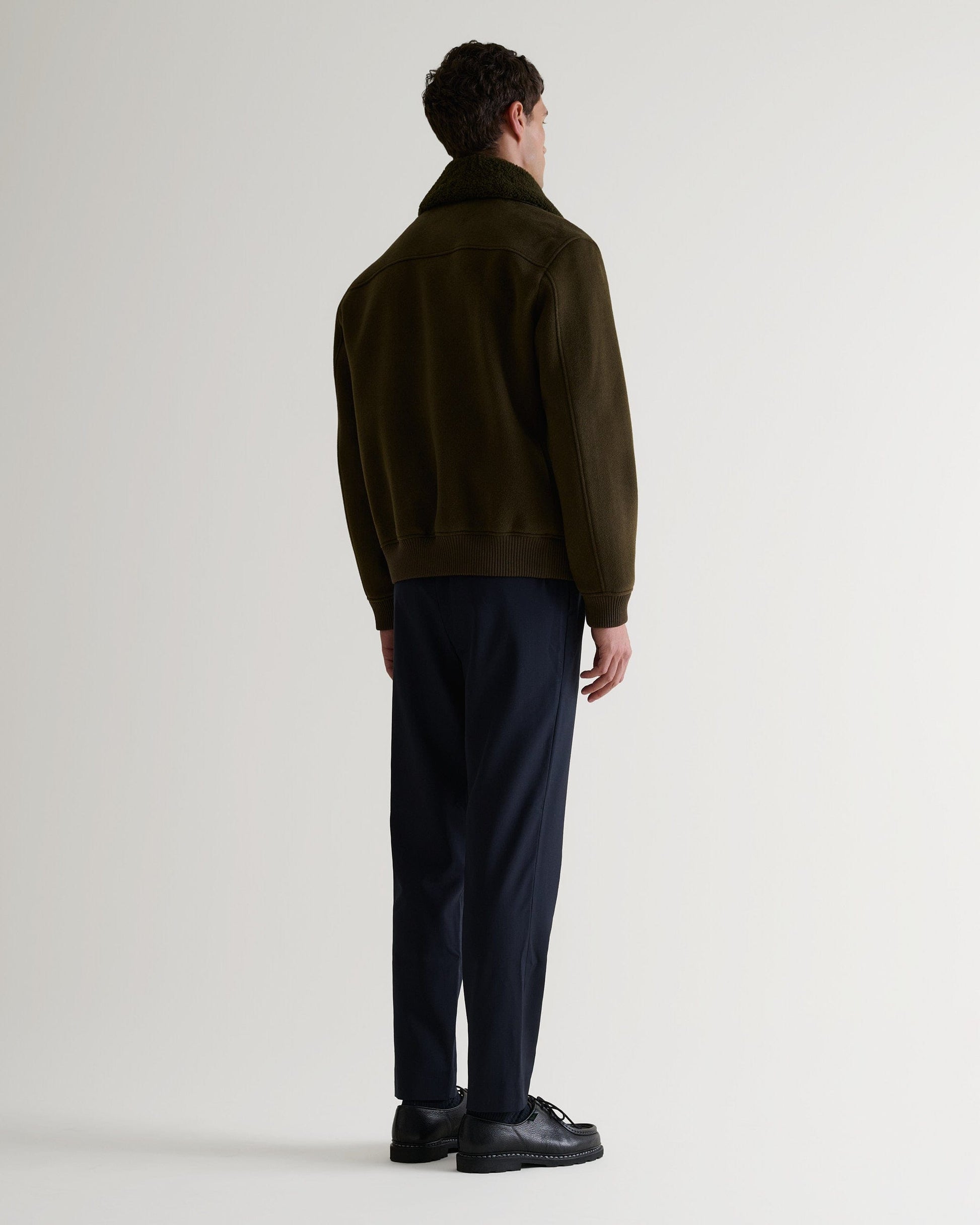 Full length back view of Rise & Fall's olive wool bomber jacket with shearling collar.