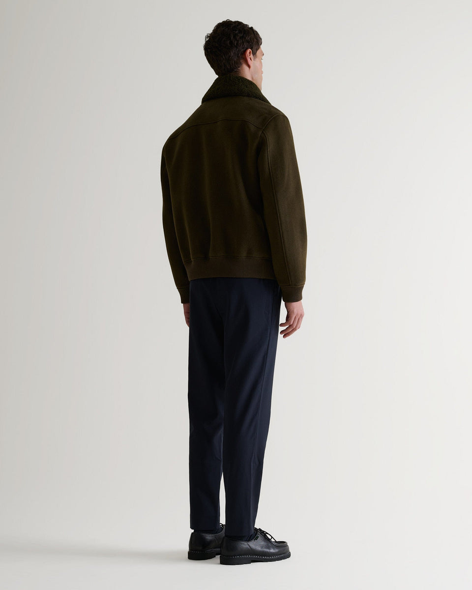 Full length back view of Rise & Fall's olive wool bomber jacket with shearling collar.