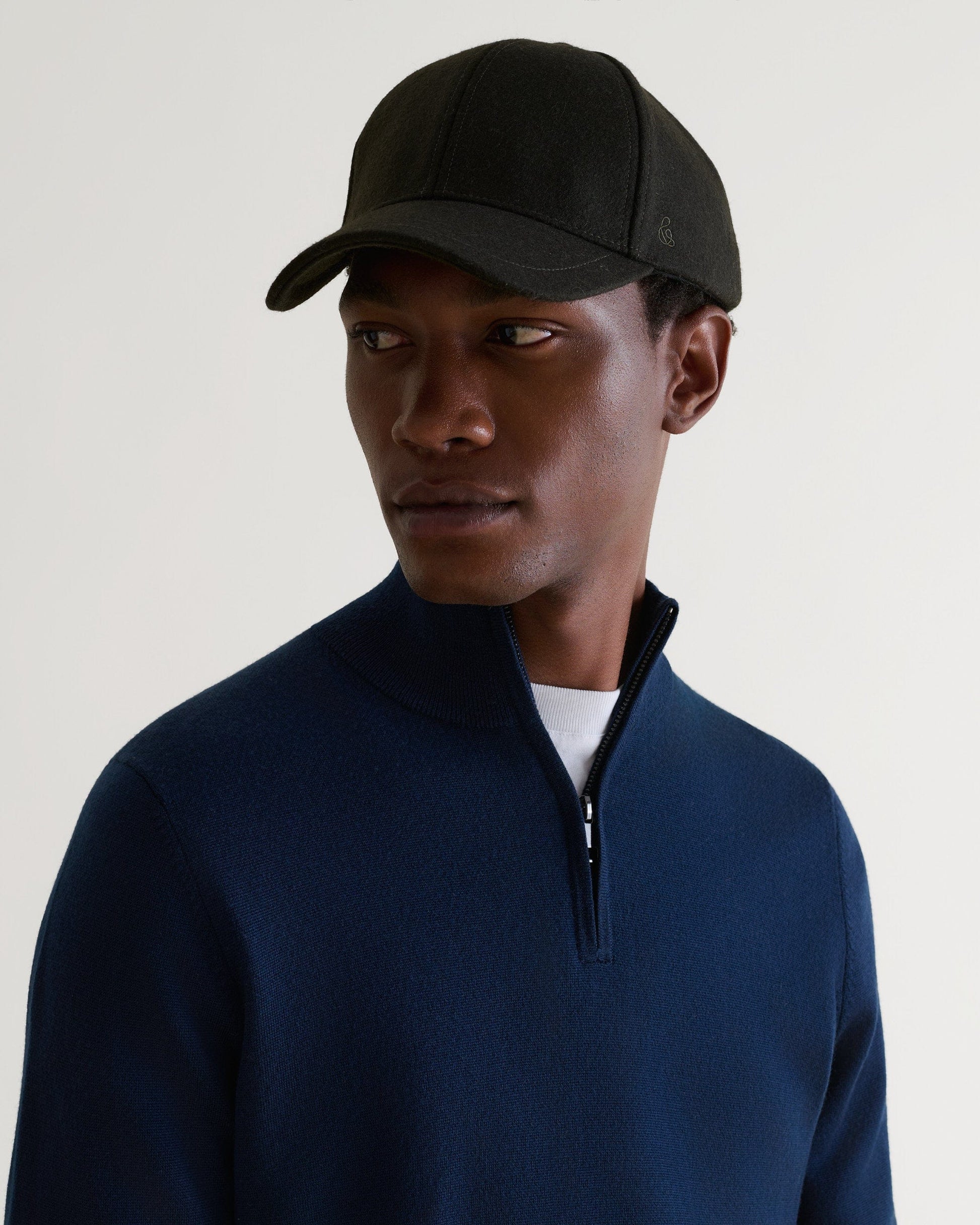 Side view of man wearing military green cashmere wool baseball cap with a white T-shirt and blue zip cashmere jumper.