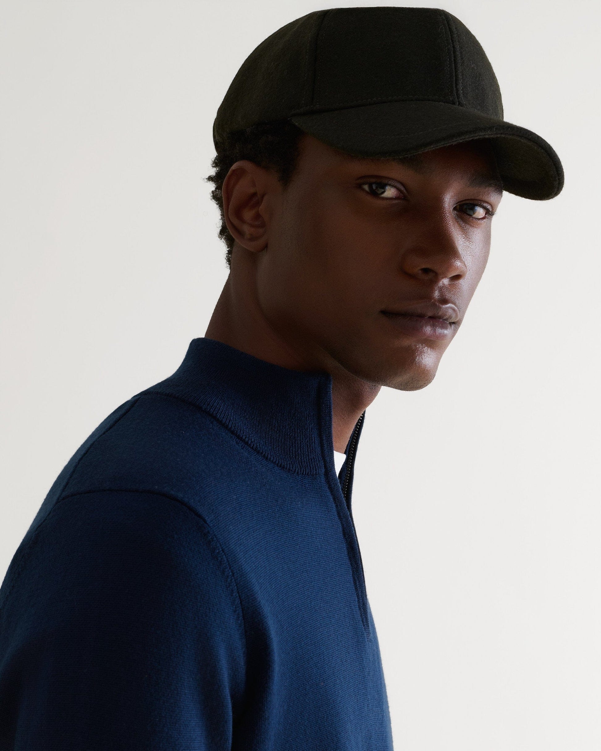 Side view of man wearing military green cashmere merino wool baseball cap with a white T-shirt and blue cashmere jumper.