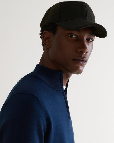 Side view of man wearing military green cashmere merino wool baseball cap with a white T-shirt and blue cashmere jumper.