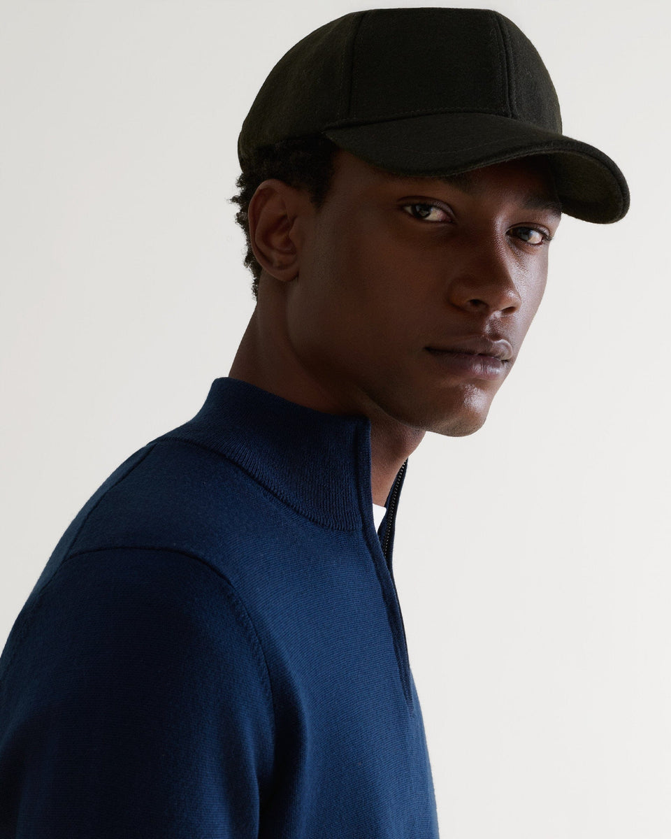 Side view of man wearing military green cashmere merino wool baseball cap with a white T-shirt and blue cashmere jumper.