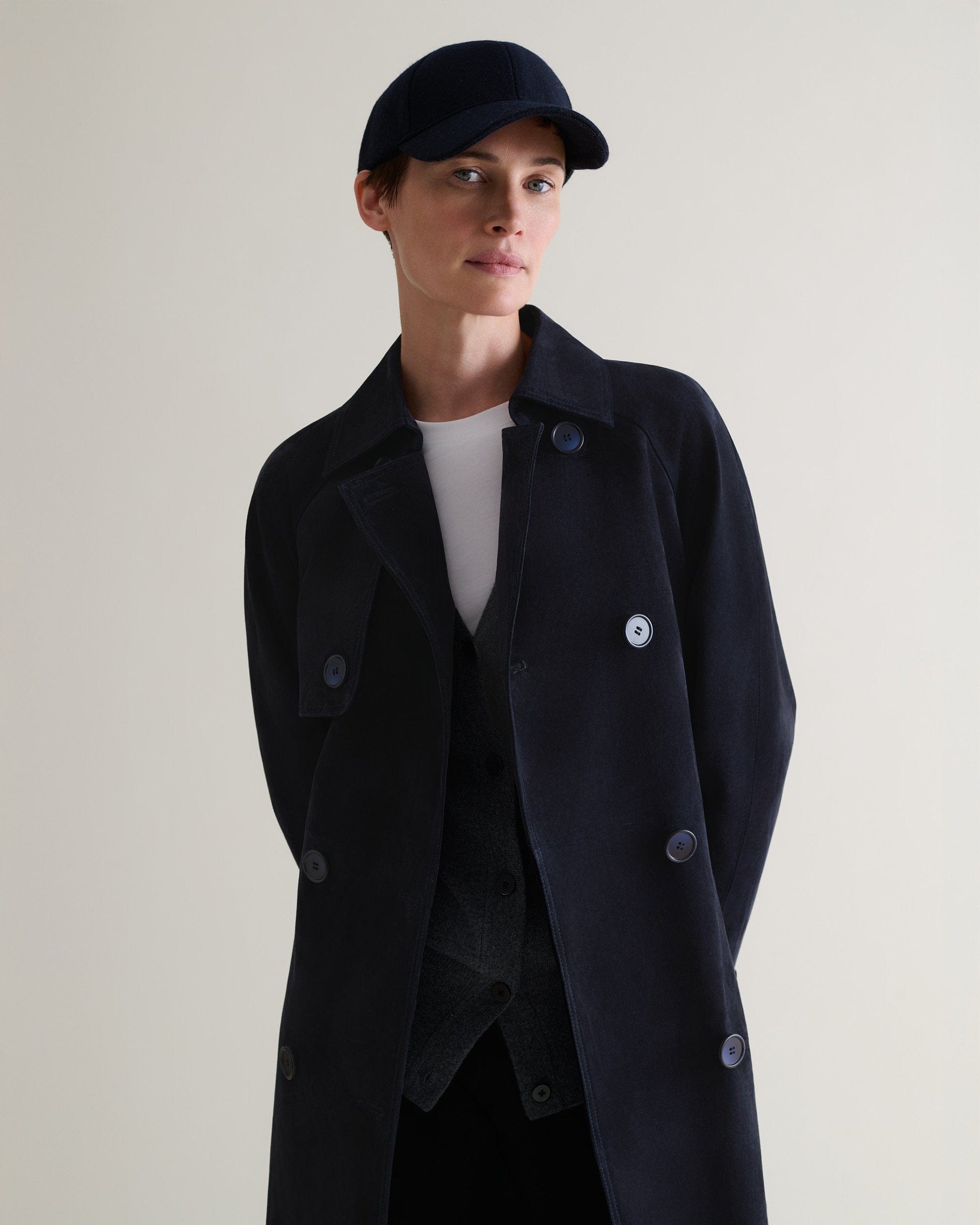 Woman wearing navy cashmere merino wool baseball cap with matching suede trench coat and white t-shirt.