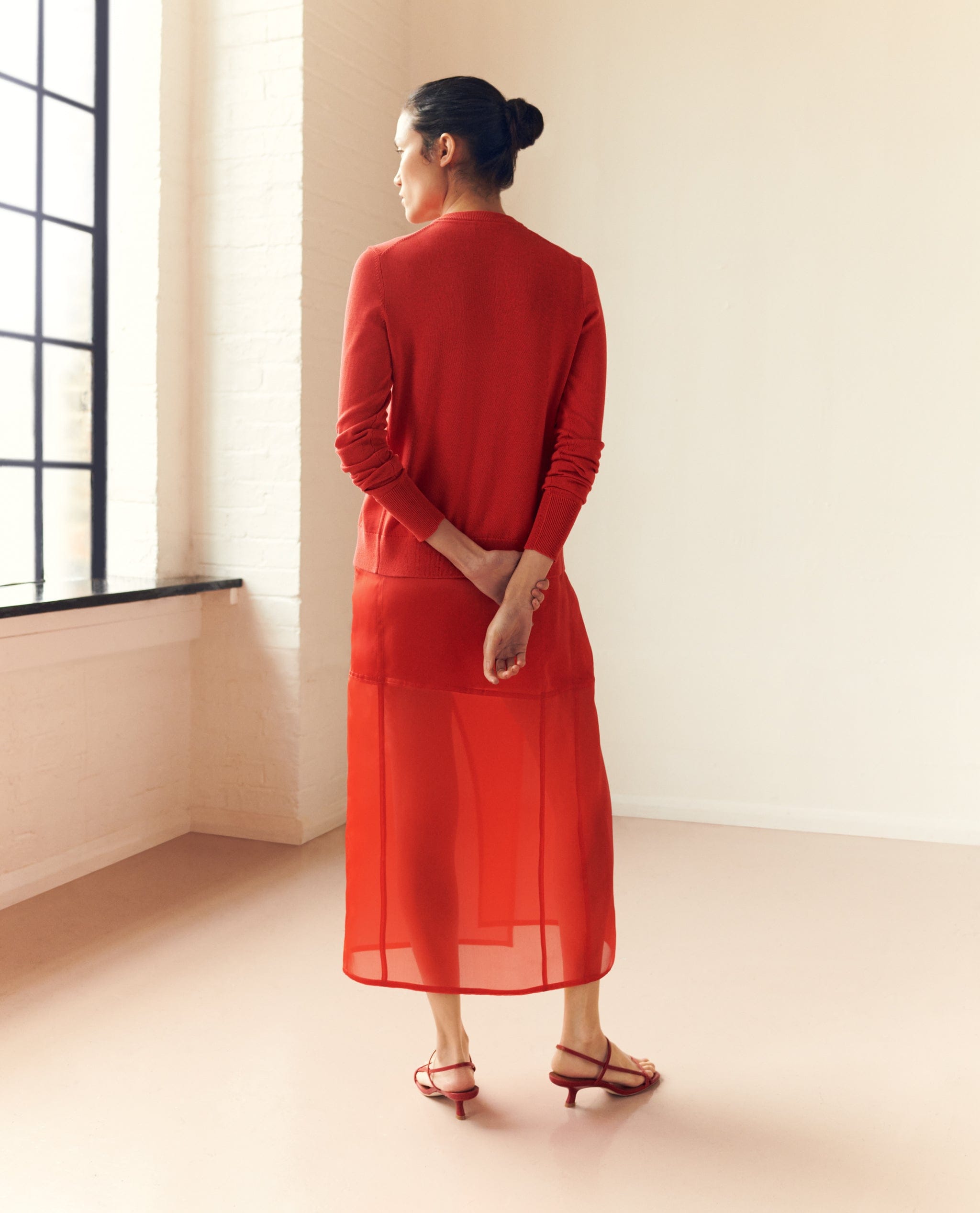 Back of woman wearing red silk organza panelled skirt with matching red cardigan.