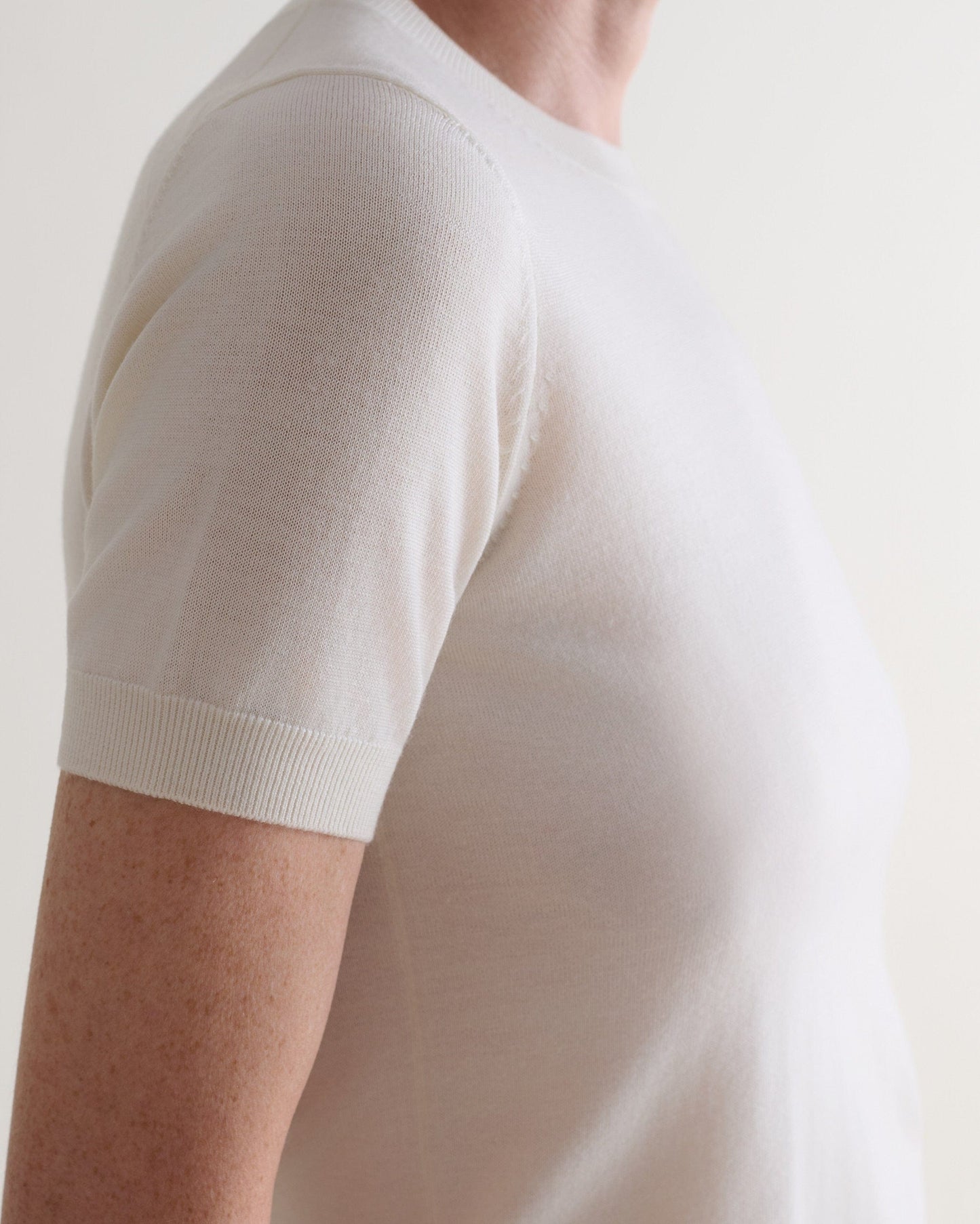 Close up side view of woman wearing Rise & Fall's cream superfine merino wool knitted t-shirt. 