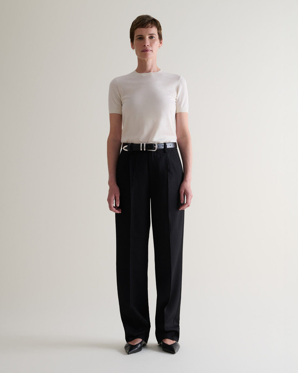 Front view of woman wearing Rise & Fall's cream superfine merino wool knitted t-shirt. Worn with black trousers and belt.
