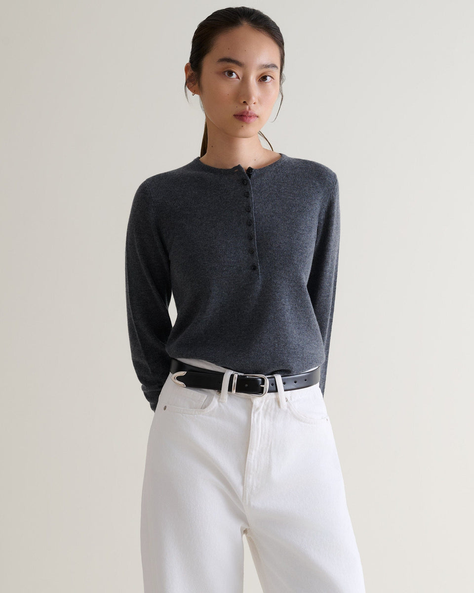 Front view of woman wearing Rise & Fall's graphite cashmere merino henley jumper. Worn with white jeans and black belt.