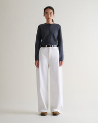 Full length front view of woman wearing Rise & Fall's graphite cashmere merino henley jumper. Worn with wide white jeans.