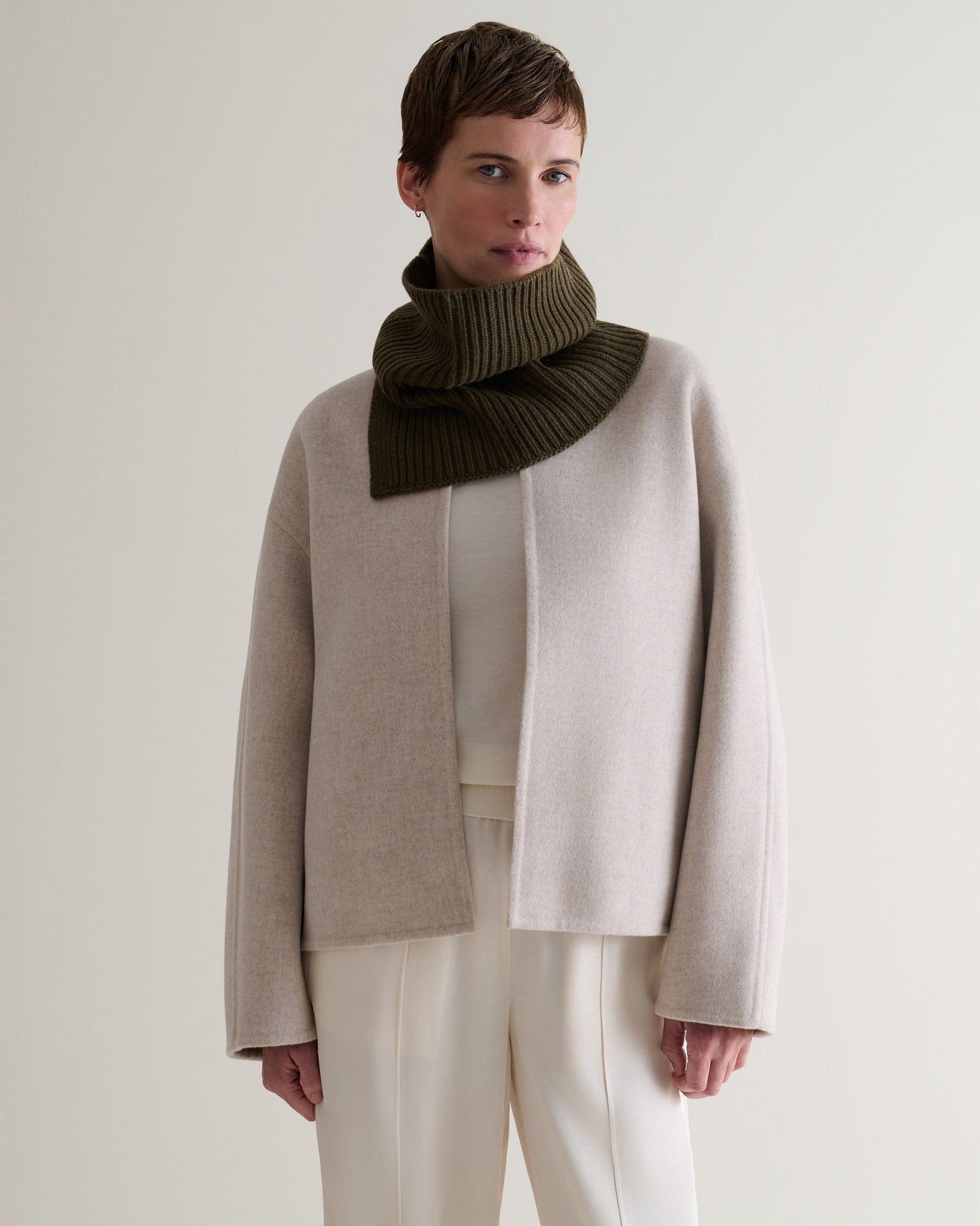 Woman wearing Rise & Fall's cashmere merino ribbed collar in military green over a cream jumper and light grey jacket