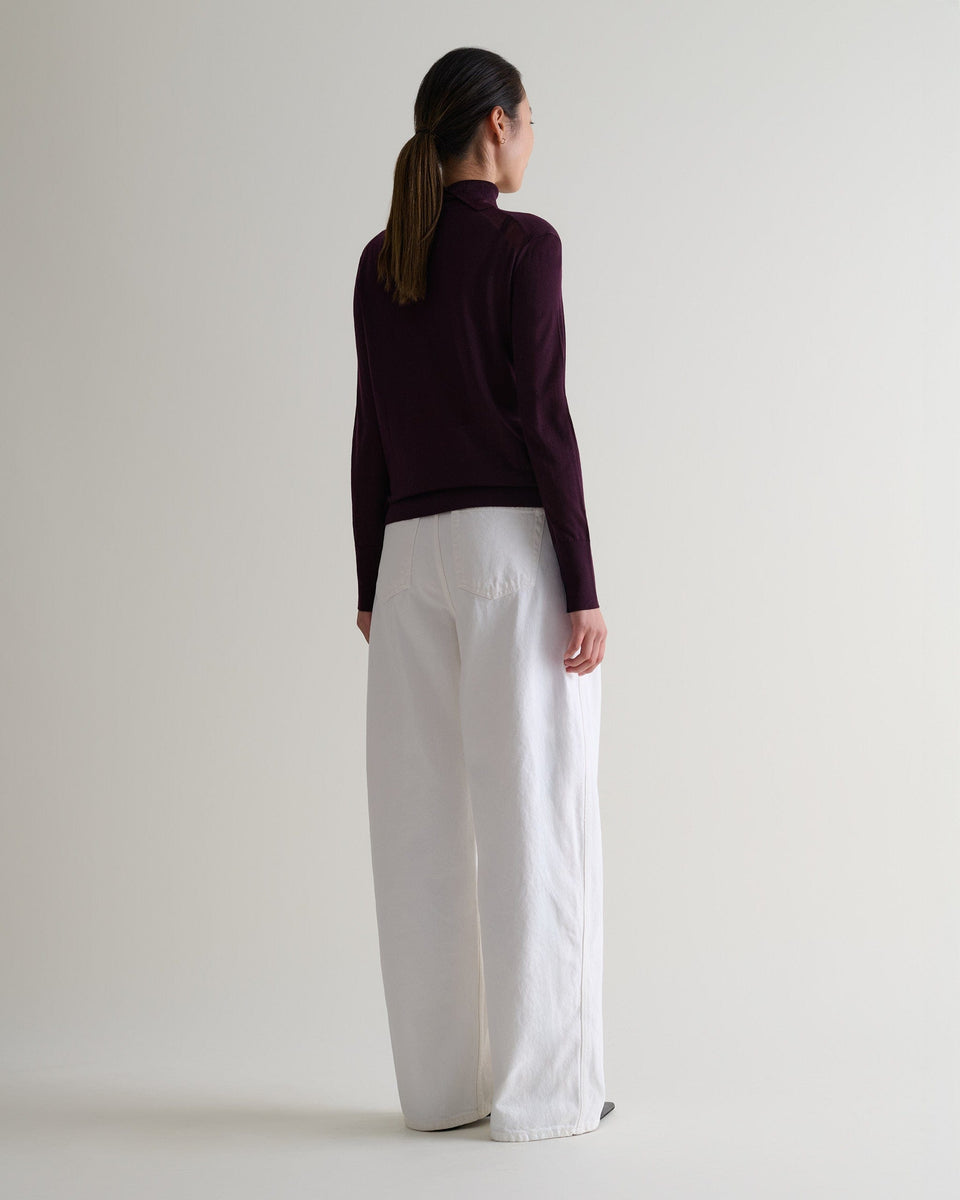 Full length back view of woman wearing Rise & Fall's oxblood superfine merino roll neck jumper. Worn with wide white jeans.