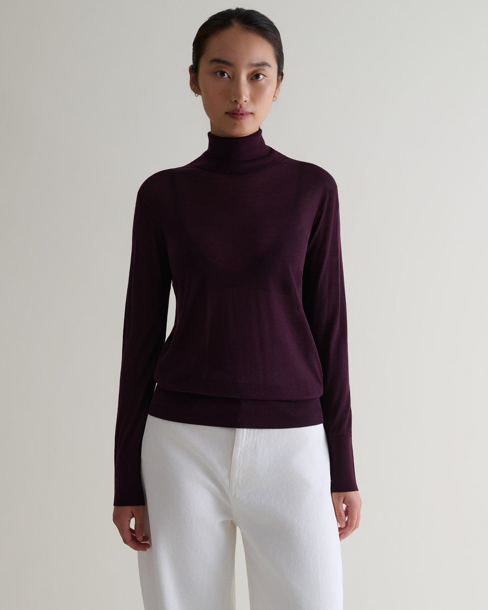 Woman wears Rise & Fall's oxblood superfine merino roll neck jumper. Worn with white jeans.