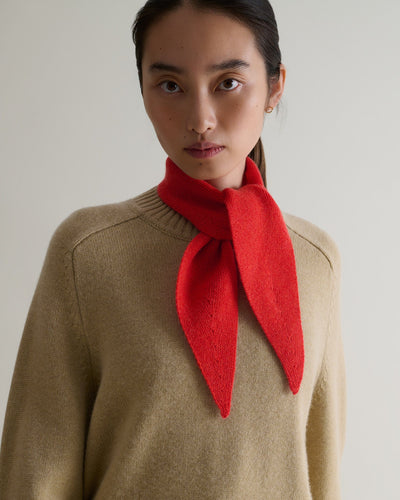 Woman wears Rise & Fall's poppy red finest cashmere ribbed micro bandana. Worn with beige crew neck jumper. 